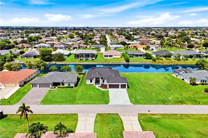 Waterfront property with expansive green lawn, mature landscaping, and a paver driveway