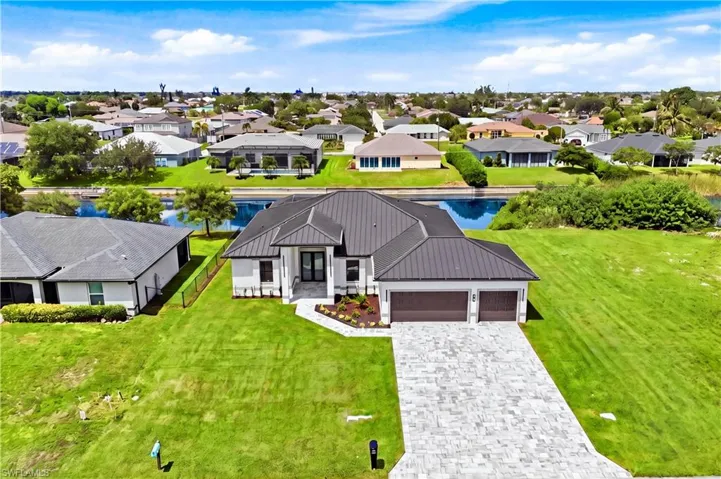 Modern exterior with a dark metal roof, paver driveway, and two-car garage