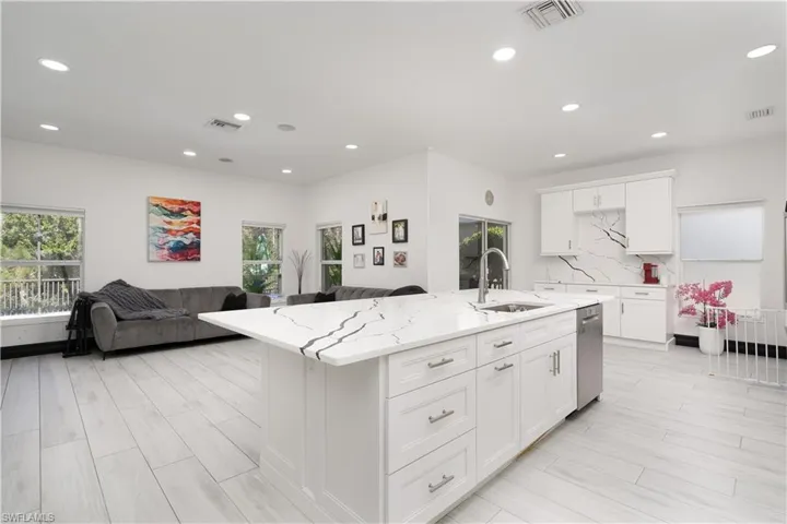 Kitchen featuring white cabinets, open floor plan, light stone counters, an island with sink, and recessed lighting