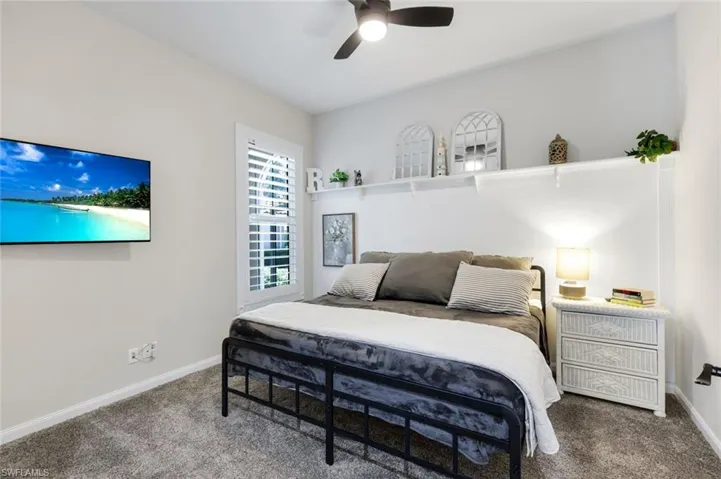 Plush carpeting, a ceiling fan with integrated lighting, wall-mounted shelving, and window shutters
