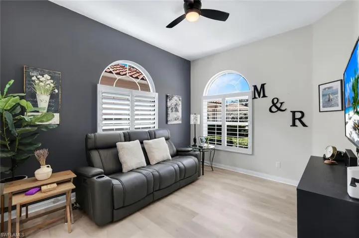 Arched windows with plantation shutters, wood-finish flooring, ceiling fan, and distinct accent wall