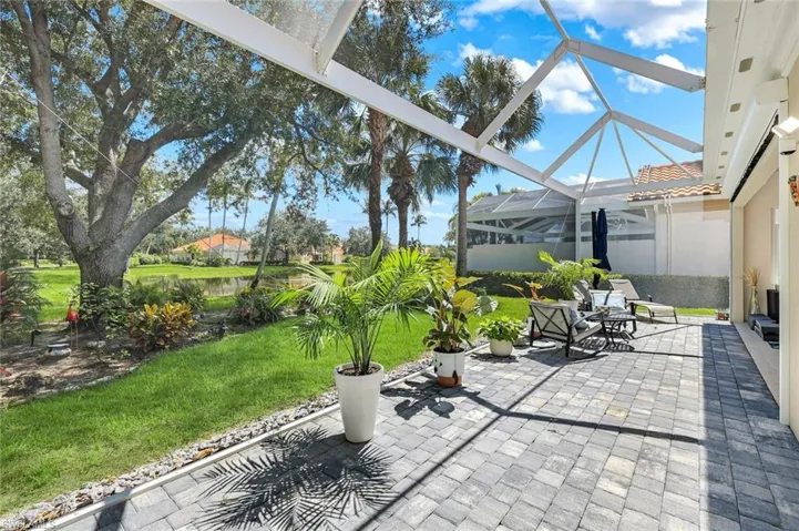 Screened patio enclosure with a paver surface, expansive green lawn, and mature trees