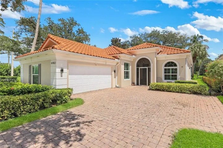 Mediterranean-inspired architecture with a barrel tile roof, arched entryway, arched window, and a paver driveway