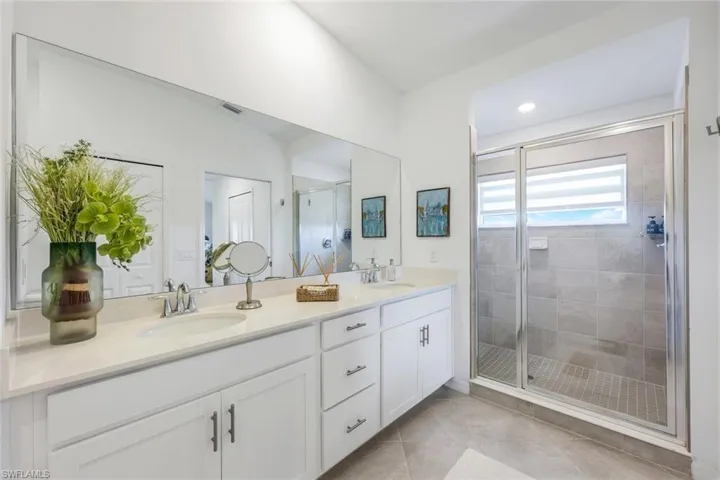 Bathroom with double vanity, a shower stall, and light tile patterned flooring