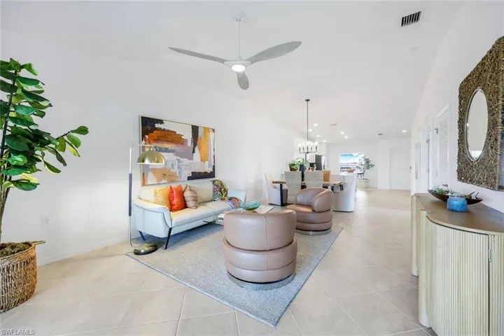 Living room with lofted ceiling, ceiling fan, light tile patterned flooring, and a chandelier