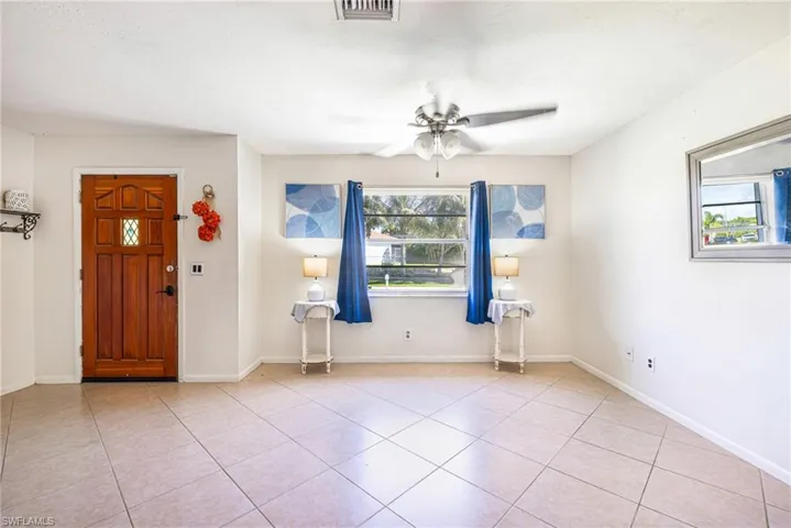 Spacious living area with ceiling fan, light wood-finish flooring, and white wall finishes