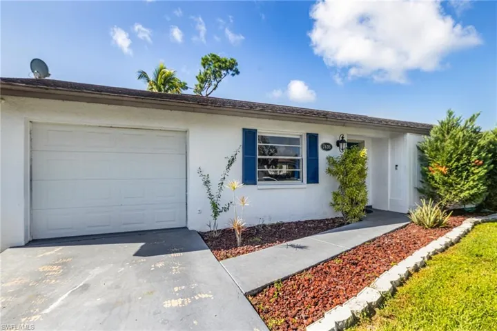 White stucco exterior with dark shutters, paneled entry door with decorative glass, and a covered entryway