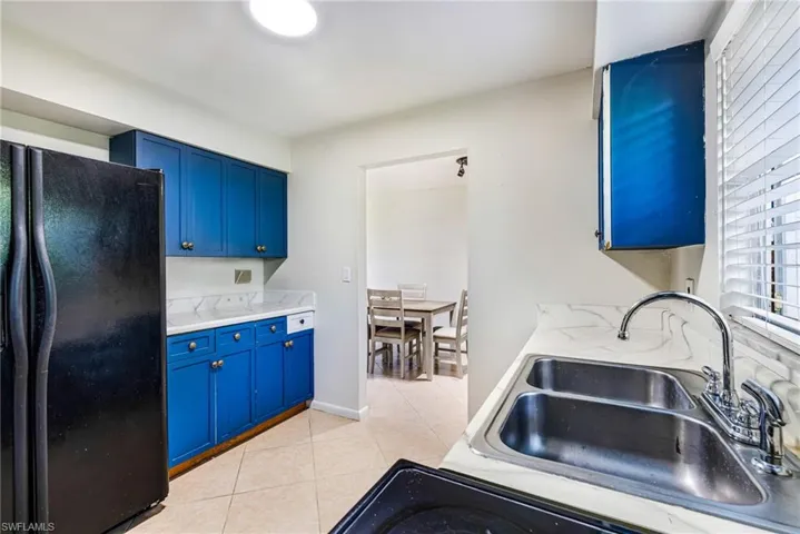 Blue cabinetry with gold-tone hardware, white stone-look countertops, stainless steel double-basin sink, and a black electric range
