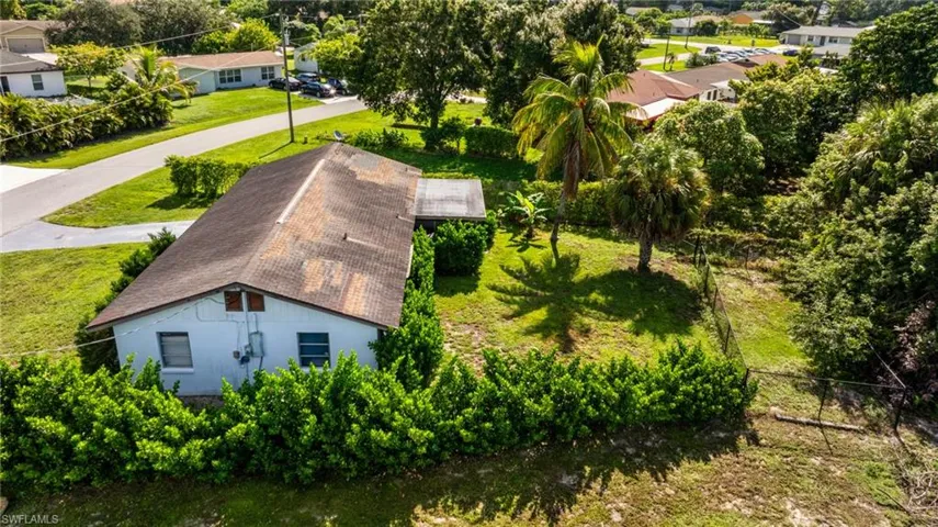 Pitched roof residence with mature perimeter shrubbery, a fenced rear yard, and established palm trees