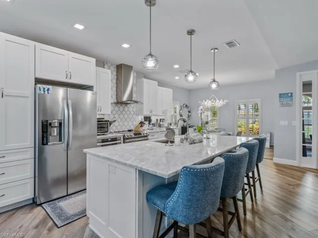 Kitchen featuring appliances with stainless steel finishes, wall chimney exhaust hood, a kitchen bar, white cabinets, and light wood finished floors