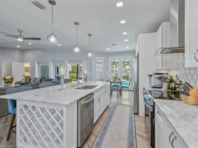 Kitchen featuring wall chimney range hood, stainless steel appliances, french doors, white cabinetry, and a center island with sink