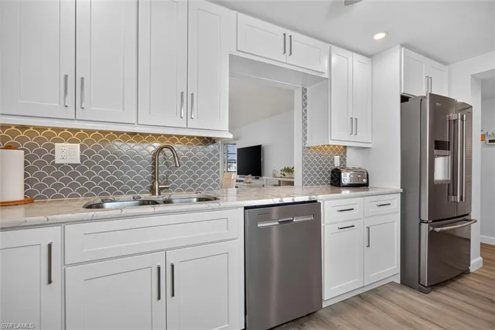 Kitchen featuring white shaker cabinetry, stainless steel appliances, marble-look countertops, a scallop-patterned backsplash, and wood-finish flooring
