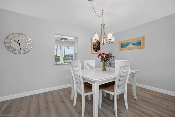 Dining area featuring wood-finish flooring, a contemporary chandelier, and a pass-through window