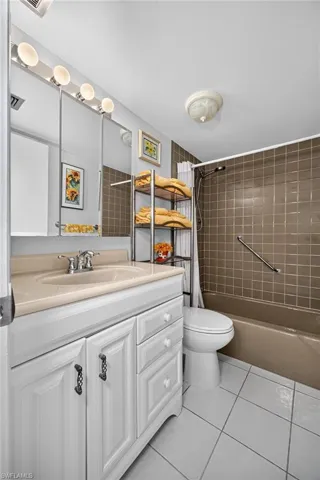 Full Guest Bathroom featuring a white vanity with a tan countertop and integrated sink, a built-in tub with brown wall tiling, and white floor tiling
