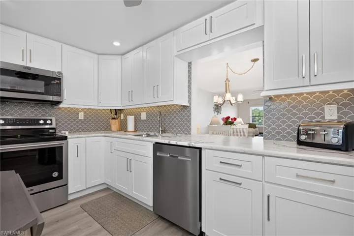 Kitchen featuring white cabinetry, stainless steel appliances, a scalloped tile backsplash, and light-toned countertops