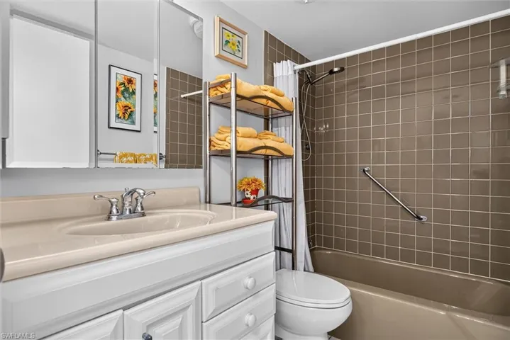 Full Guest Bathroom featuring an integrated sink vanity with white cabinetry, a three-panel mirrored medicine cabinet, a tiled shower surround, and a built-in grab bar
