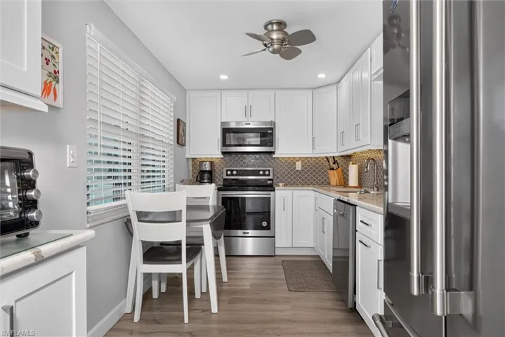 Kitchen featuring white cabinetry, stainless steel appliances, wood-finish flooring, a mosaic tile backsplash, and recessed lighting