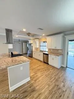 Kitchen with ornamental molding, white cabinets, healthy amount of natural light, light wood-style flooring, and extractor fan