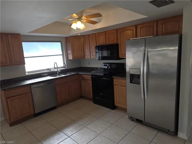 Kitchen featuring black appliances, brown cabinets, a raised ceiling, and a ceiling fan
