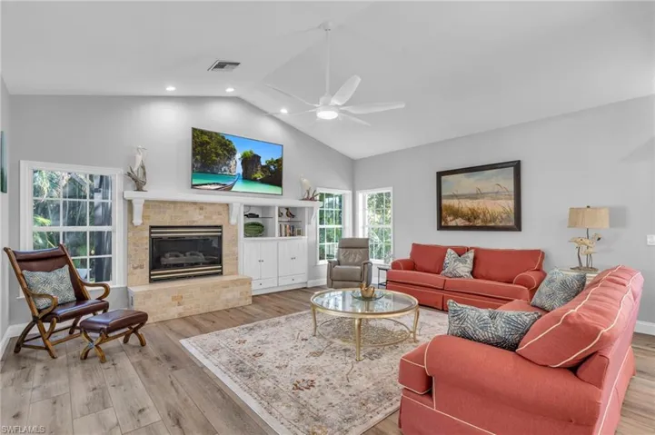 Living room featuring light wood-Look floors, a brick fireplace, ceiling fan, and vaulted ceiling