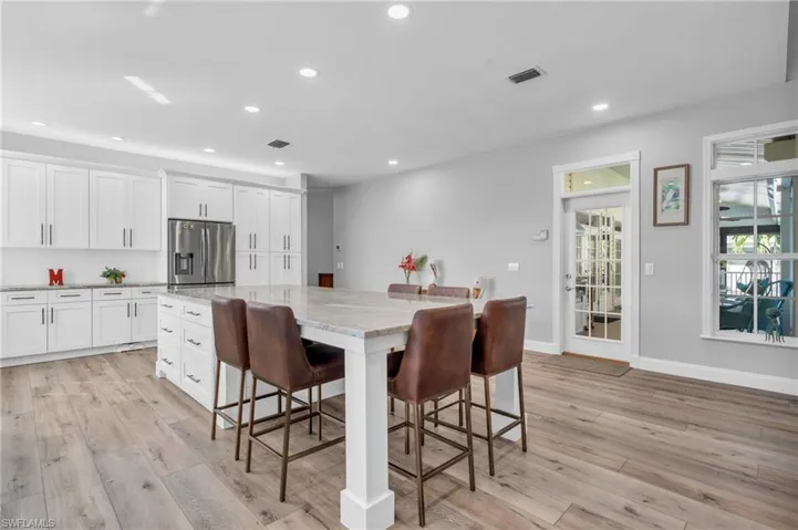 New Kitchen with light  wood-look flooring, stainless steel fridge, white cabinets, and a kitchen island