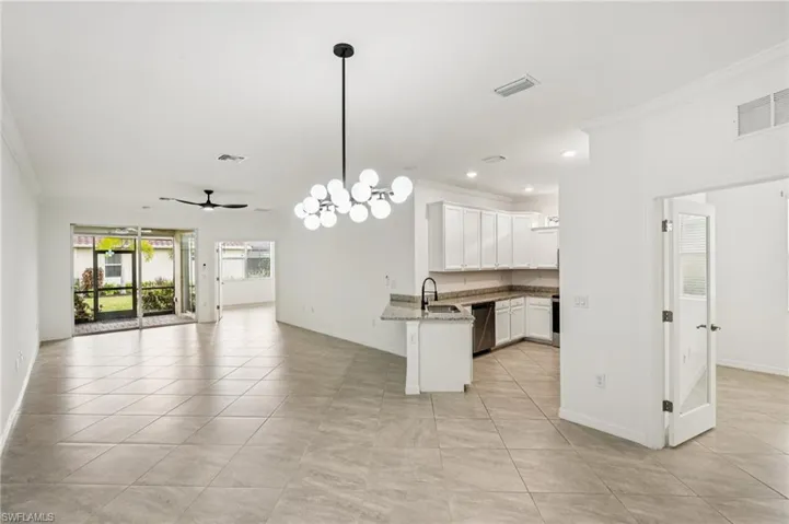 Kitchen with a chandelier, open floor plan, ornamental molding, white cabinets, and pendant lighting