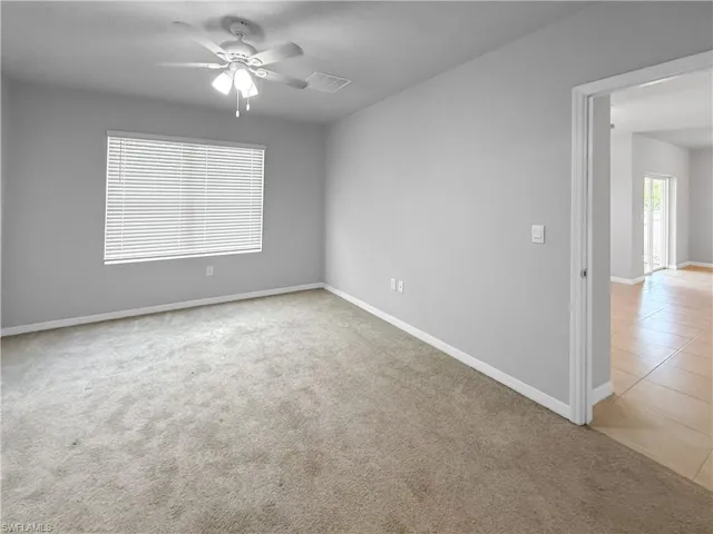 Empty room featuring light carpet, a ceiling fan, and light tile patterned floors
