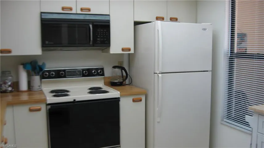 Kitchen with electric stove, white cabinetry, and white fridge