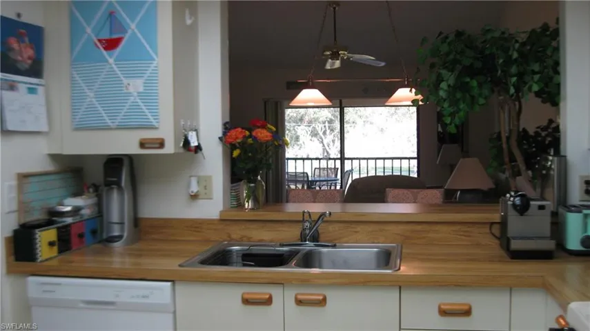 Kitchen featuring white cabinetry, butcher block countertops, sink, and dishwasher View toward lanai and landscaping.