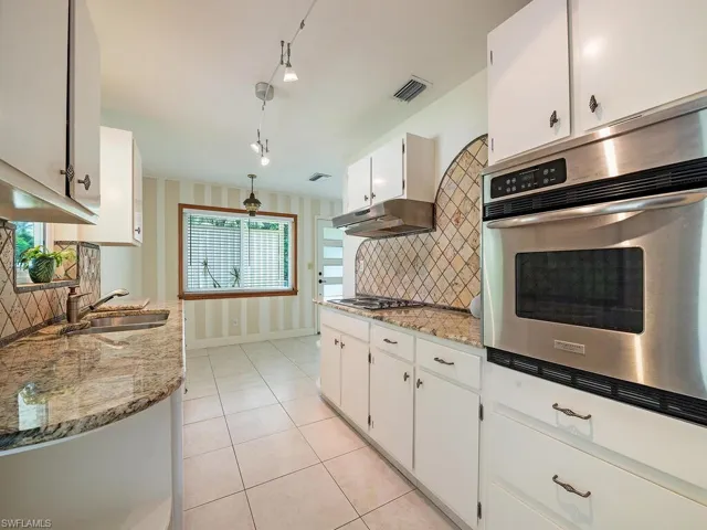 Kitchen featuring appliances with stainless steel finishes, tasteful backsplash, white cabinets, and light stone counters