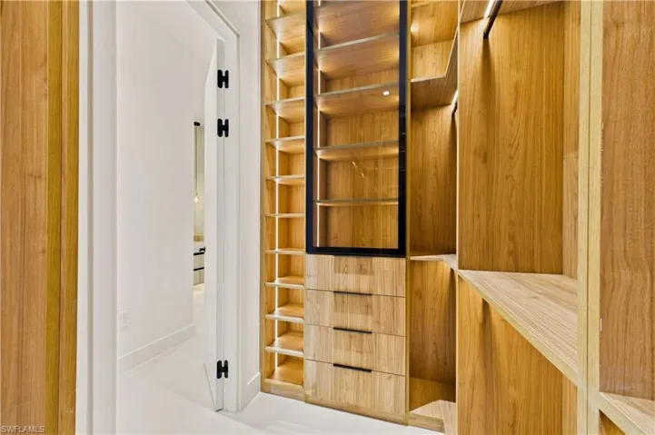 Luxurious his-and-hers walk-in closets feature custom built-in cabinetry, illuminated shelving, glass display storage, and abundant space for wardrobe organization