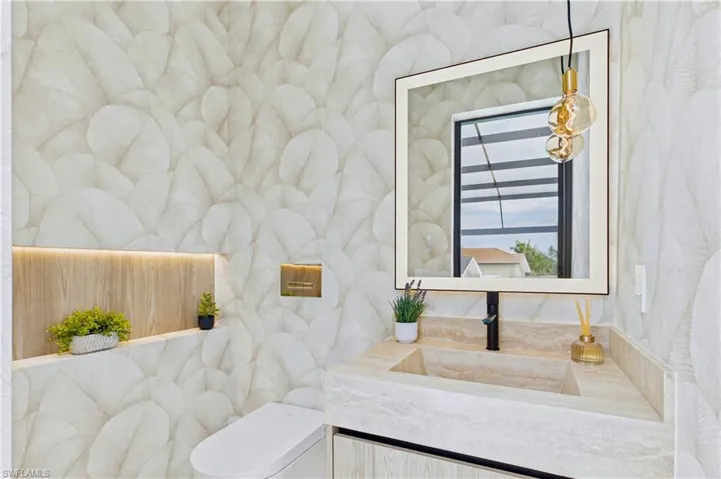 Designer cabana bath showcases custom wallpaper, an integrated stone sink, illuminated mirror, and direct access to the pool area for effortless indoor-outdoor entertaining!