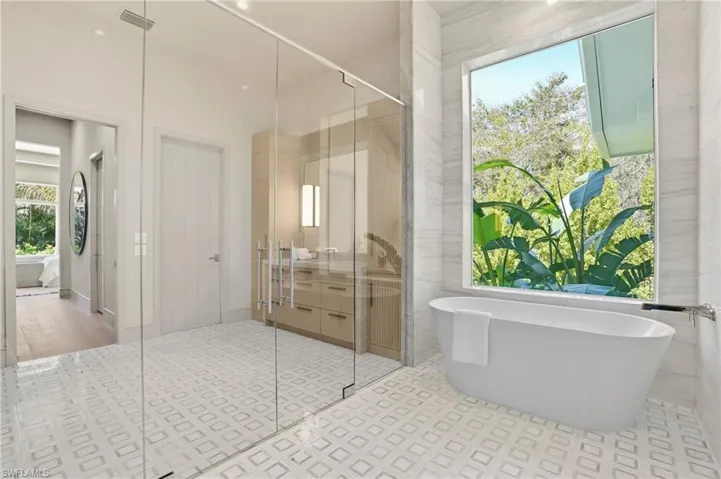 This bathroom features a freestanding soaking tub positioned beneath a large window, a spacious walk-in shower with clear glass enclosures, and a vanity with dual sinks