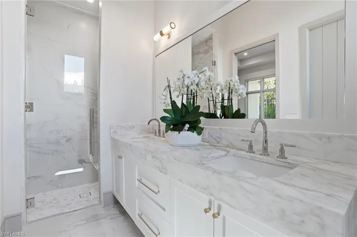 Full bathroom with double vanity, a marble finish shower, and light marble finish flooring
