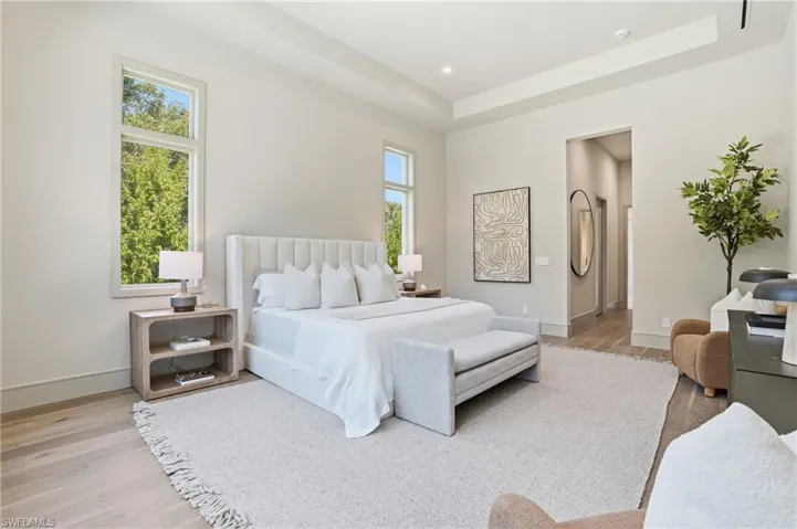 Bedroom with light wood-style flooring, a raised ceiling, ensuite bathroom, and recessed lighting