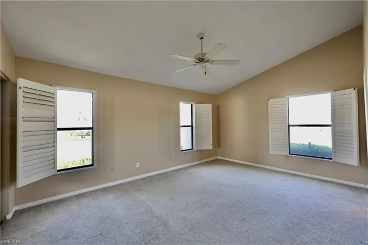Unfurnished room with a ceiling fan, light carpet, healthy amount of natural light, and vaulted ceiling
