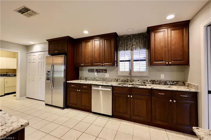 Kitchen featuring stainless steel appliances, light stone countertops, light tile patterned flooring, recessed lighting, and dark wood finish cabinetry