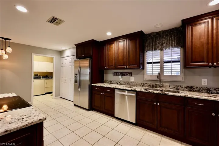 Kitchen with stainless steel appliances, light stone counters, dark wood finish cabinetry, and decorative light fixtures