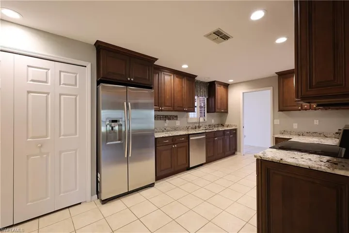 Kitchen with stainless steel appliances, dark wood finish cabinets, light stone counters, recessed lighting, and light tile patterned floors