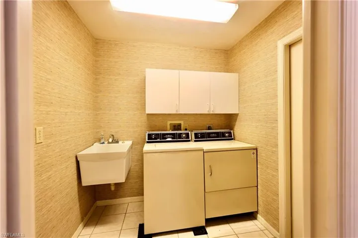 Laundry room with wallpapered walls, washer and dryer, light tile patterned floors, and cabinet space