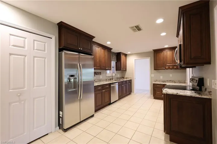 Kitchen featuring stainless steel appliances, light stone counters, dark wood finish cabinets, recessed lighting, and light tile patterned floors