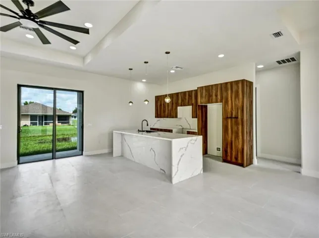 Open-concept living space with large sliding glass doors, a kitchen island featuring a waterfall edge, wood-finish cabinetry, and recessed lighting