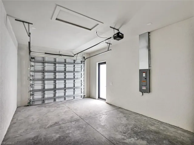 Spacious garage featuring a concrete floor, a roll-up garage door, a side entry door, and an overhead lighting fixture