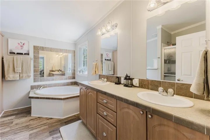 Bathroom with crown molding, a stall shower, double vanity, wood finished floors, and a garden tub