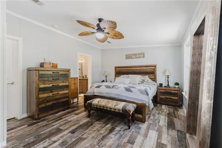 Bedroom with crown molding, dark wood-type flooring, a ceiling fan, and ensuite bath
