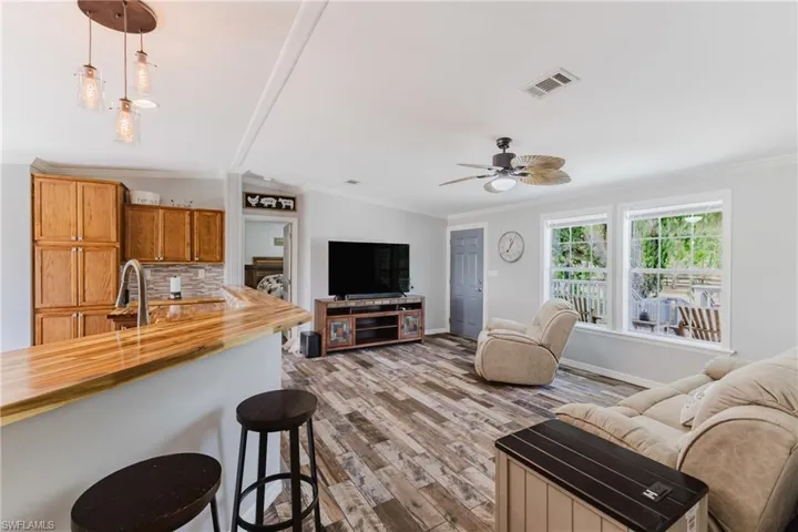 Living area featuring ornamental molding, vaulted ceiling, wood finished floors, ceiling fan, and baseboards