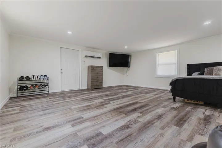 Bedroom featuring ornamental molding, a wall unit AC, wood finished floors, baseboards, and recessed lighting