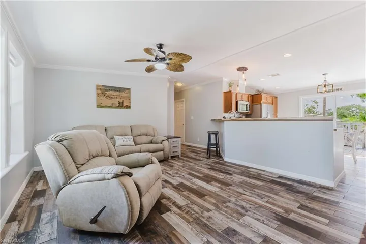 Living area featuring crown molding, dark wood-type flooring, baseboards, a ceiling fan, and recessed lighting
