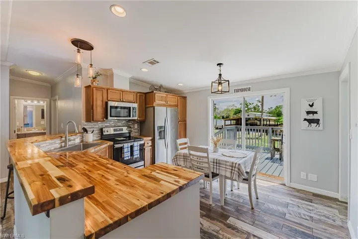 Kitchen featuring appliances with stainless steel finishes, butcher block countertops, baseboards, dark wood-type flooring, and tasteful backsplash