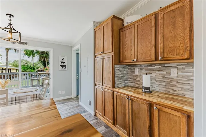 Kitchen with butcher block countertops, ornamental molding, light wood-type flooring, decorative backsplash, and a chandelier